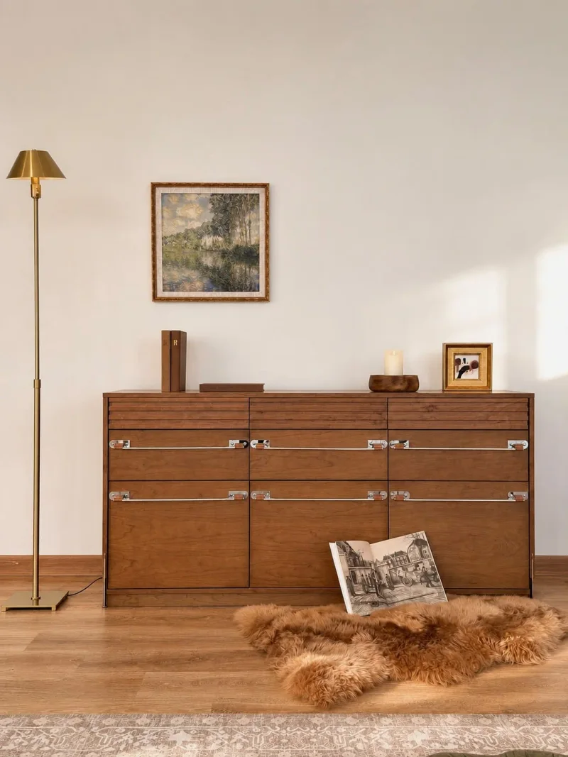 Timber sideboard beneath framed art, with a floor lamp and a pelt in the foreground.